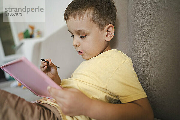 Boy using graphic tablet sitting on sofa at home