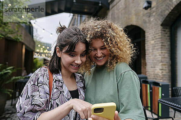 Happy lesbian couple using smart phone near building