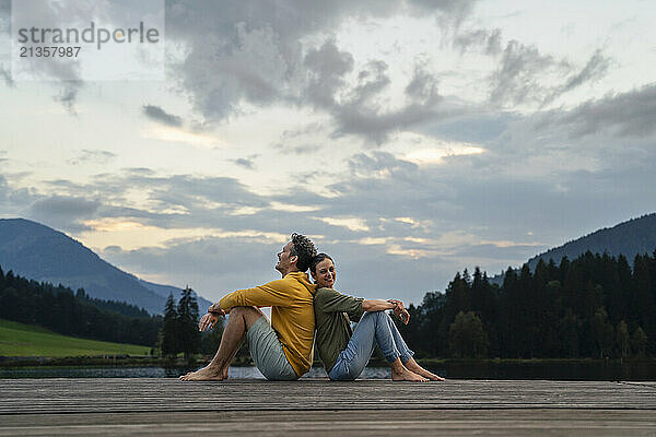 Smiling mature couple sitting back to back on jetty