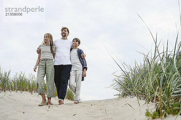 Father with son and daughter walking on sand at beach