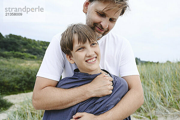 Smiling father embracing son at meadow