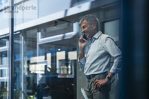 Happy senior businessman talking on smart phone seen through glass