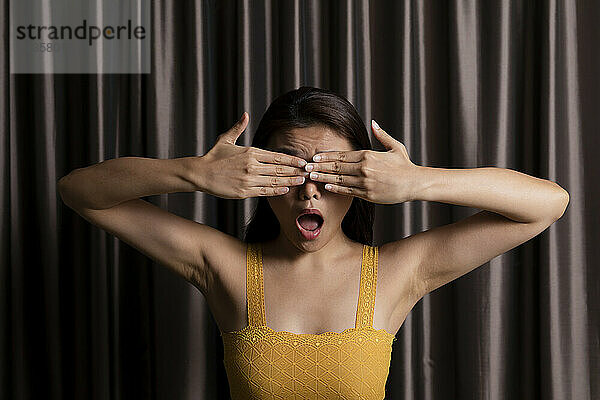 Playful woman with mouth open covering eyes in photo booth