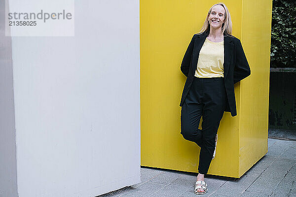 Happy businesswoman leaning on yellow wall