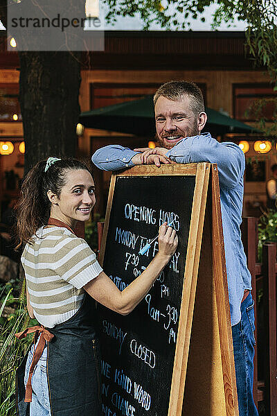 Cafe owners standing near chalkboard outside coffee shop