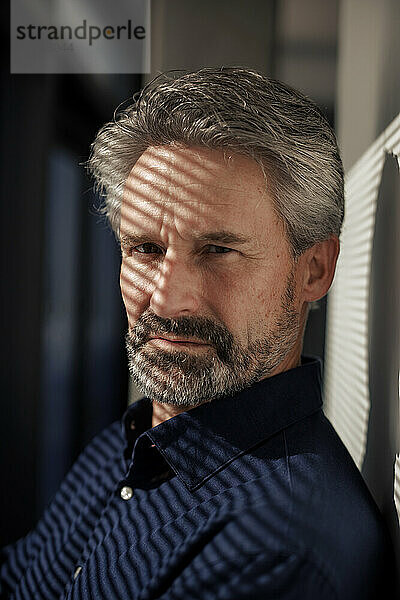 Serious senior businessman with sunlight over face near wall