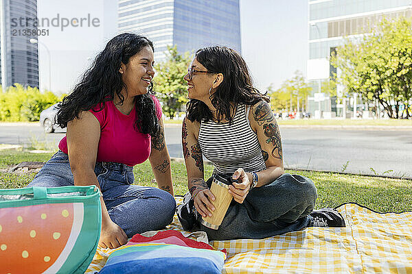 Happy lesbian couple spending leisure time sitting on picnic blanket at park