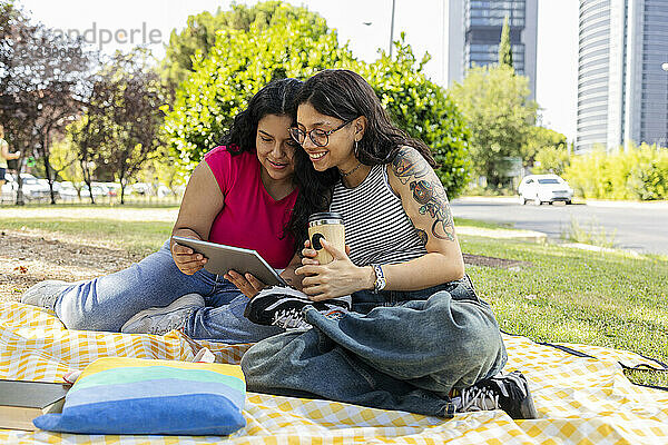 Young lesbian couple spending leisure time reading book sitting at park