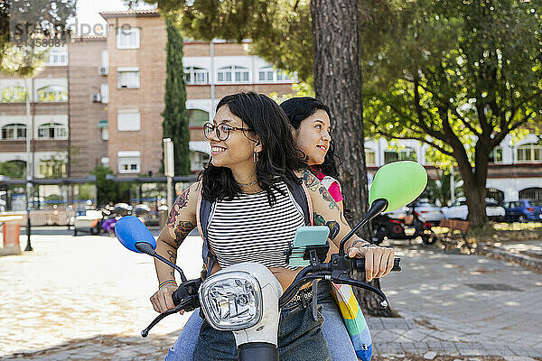 Woman sitting with girlfriend riding motor scooter at street