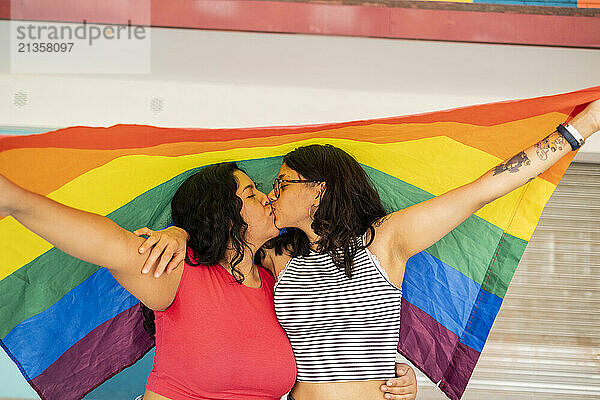 Young lesbian couple kissing and holding LQBTQIA pride flag