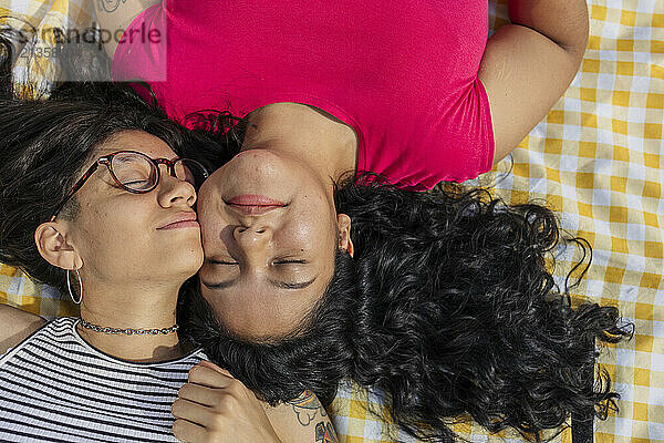 Young gay couple lying cheek to cheek on picnic blanket