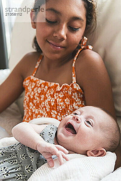 Sister looking at smiling baby girl at home