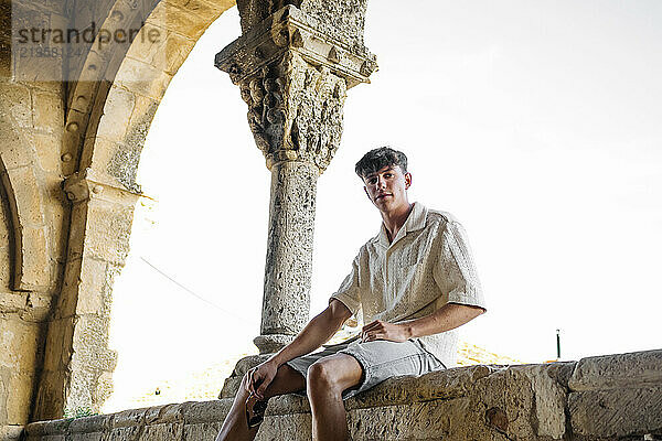 Young man sitting near ancient architectural column inside old castle