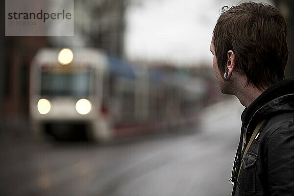 Urban man waiting for light rail train on a rainy city day downtown.