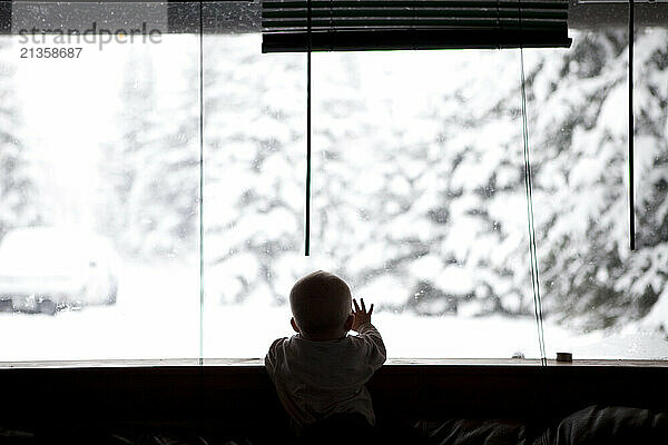 Toddler at large window looking out over snowy winter scene the day after Christmas.