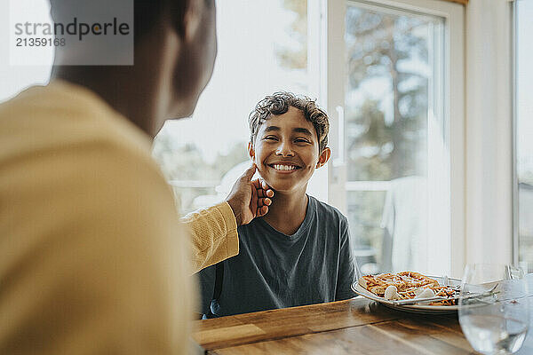 Father touching cheek of son sitting for lunch at dining table