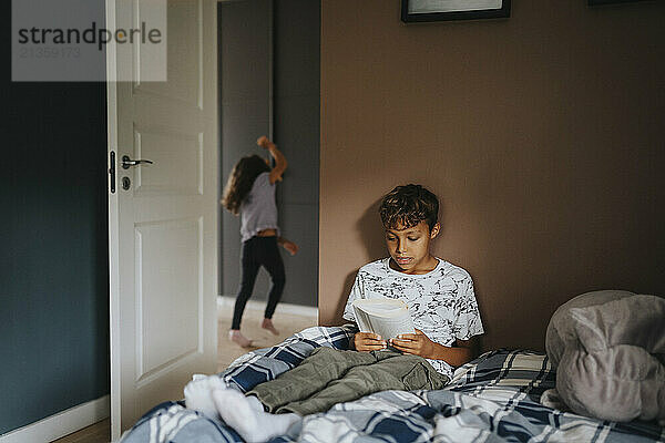 Focused boy studying while sitting on bed in bedroom at home