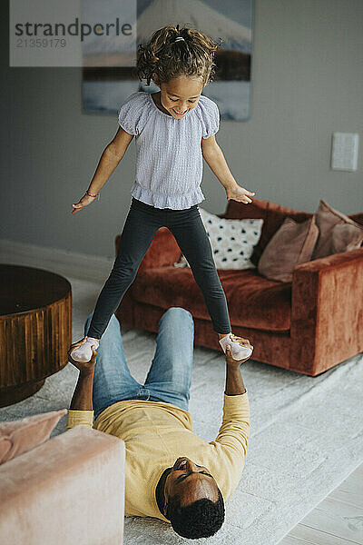 High angle view of happy girl playing with father lying on carpet at home