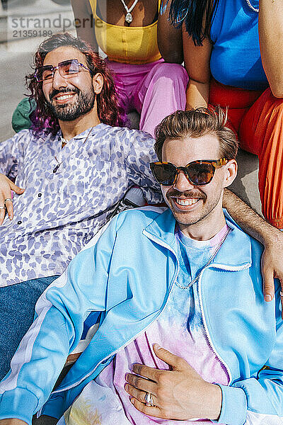 High angle view portrait of smiling fashionable man sitting with male and female friends at sunny day