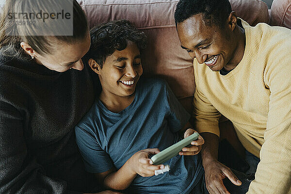 High angle view of parents sitting on sofa beside son using smart phone