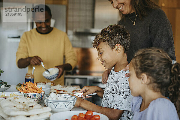 Side view of smiling boy preparing food with family in kitchen at home