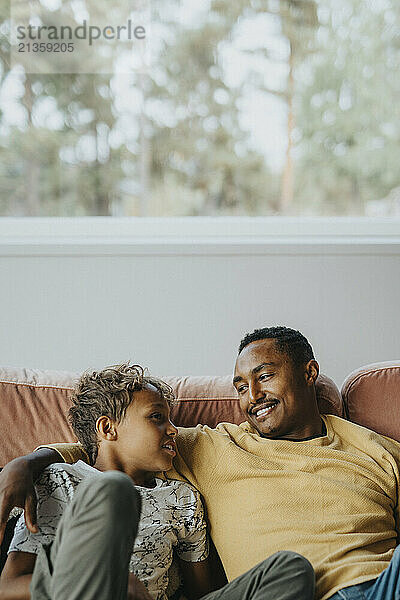 Smiling man with arm around son sitting on sofa at home