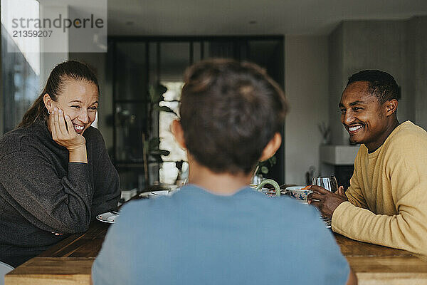 Happy parents talking with son at lunch while sitting near dining table at home