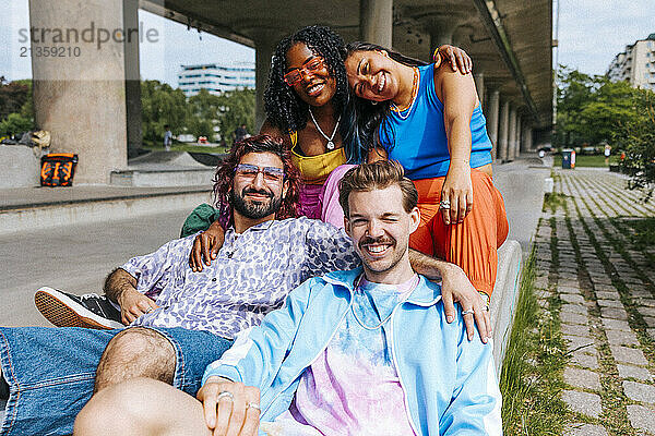 Portrait of happy fashionable male and female friends sitting near overpass under bridge