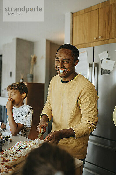 Happy mature man making pizza with family while standing in kitchen at home