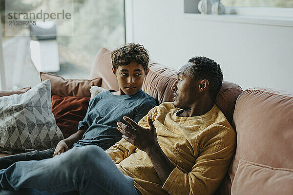 Father talking with son while sitting on sofa in living room at home