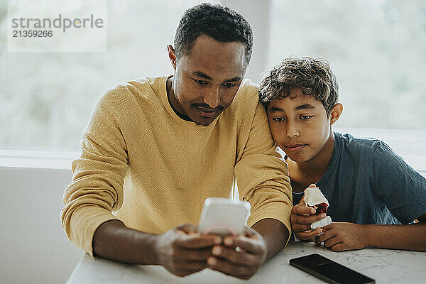 Boy sitting with father using smart phone at home