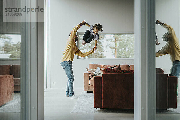 Side view of father tossing daughter in mid-air while playing in living room at home