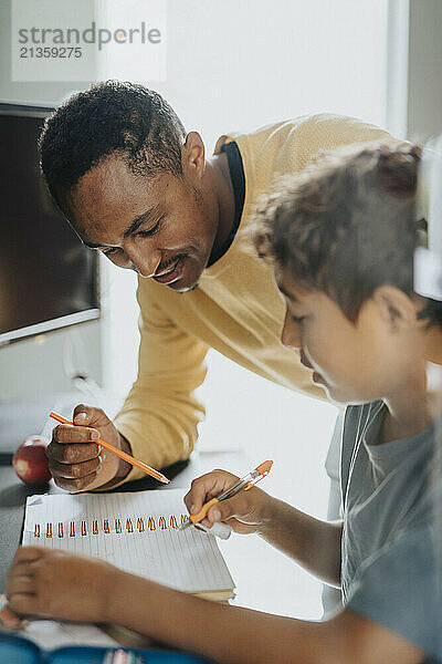 Smiling father helping son doing homework at home