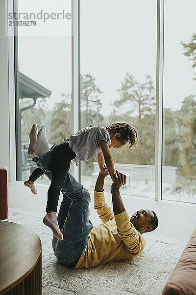 Happy man picking up daughter while lying on carpet in living room at home