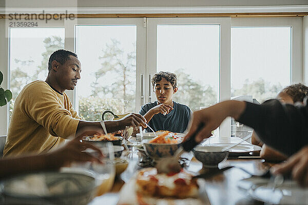 Multiracial boy having lunch with family members while sitting at dining table