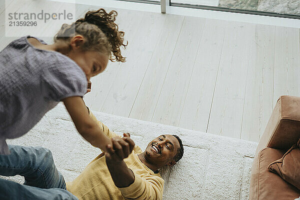 High angle view of happy man playing with daughter while lying on carpet at home