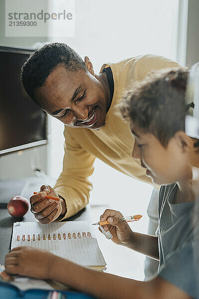 Smiling man helping son doing homework at home