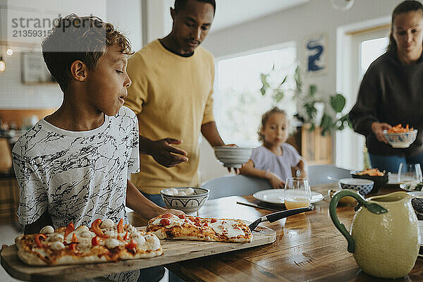 Boy keeping pizza board on dining table for lunch at home