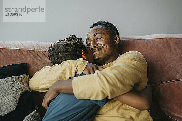 Smiling father embracing son while sitting on sofa at home