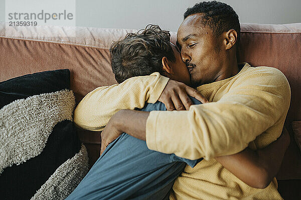 Father kissing son while sitting on sofa at home