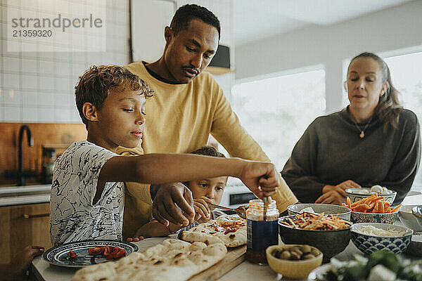 Boy making pizza with family members while standing in kitchen at home