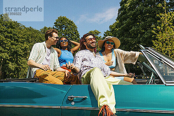 Happy fashionable male and female friends enjoying while sitting in vintage car at sunny day