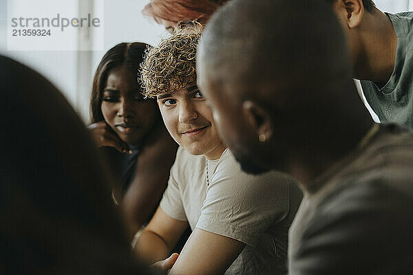 Smiling teenage boy with curly hair looking at teacher discussing at high school