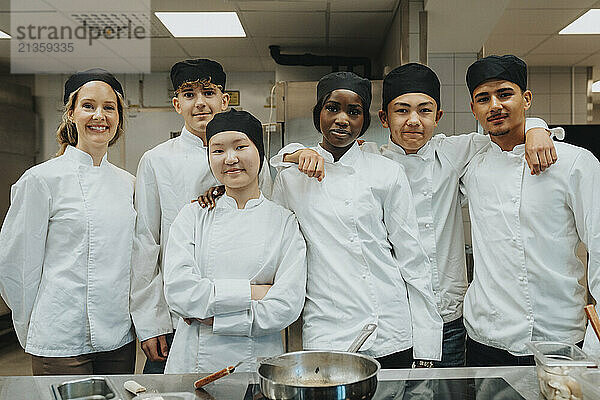 Portrait of male and female trainee standing with teacher in commercial kitchen