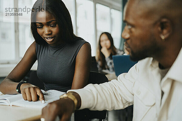 Female student reading book by male teacher in classroom