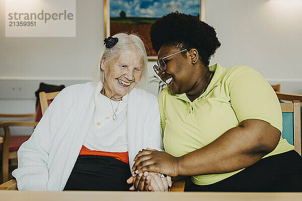 Smiling female nurse holding hands and consoling elderly female at retirement home