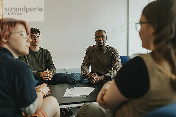 Male counselor and student looking at teenage girl discussing by non-binary person during group therapy