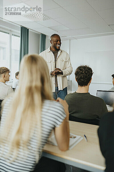 Happy male teacher gesturing while discussing with high school students in classroom