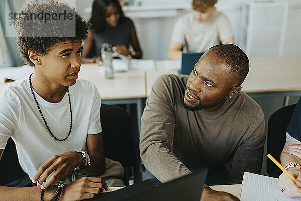 Teenage male student discussing with teacher in classroom at high school