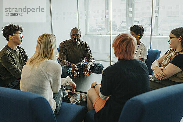 Mental health professional discussing with male and female students during group therapy